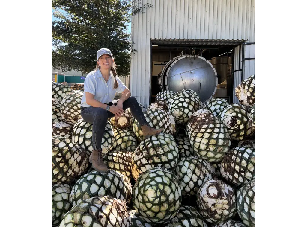Christiane, founder of Valor Tequila, sits on a pile of agave, sustainably sourced for the creation of a sustainable tequila company